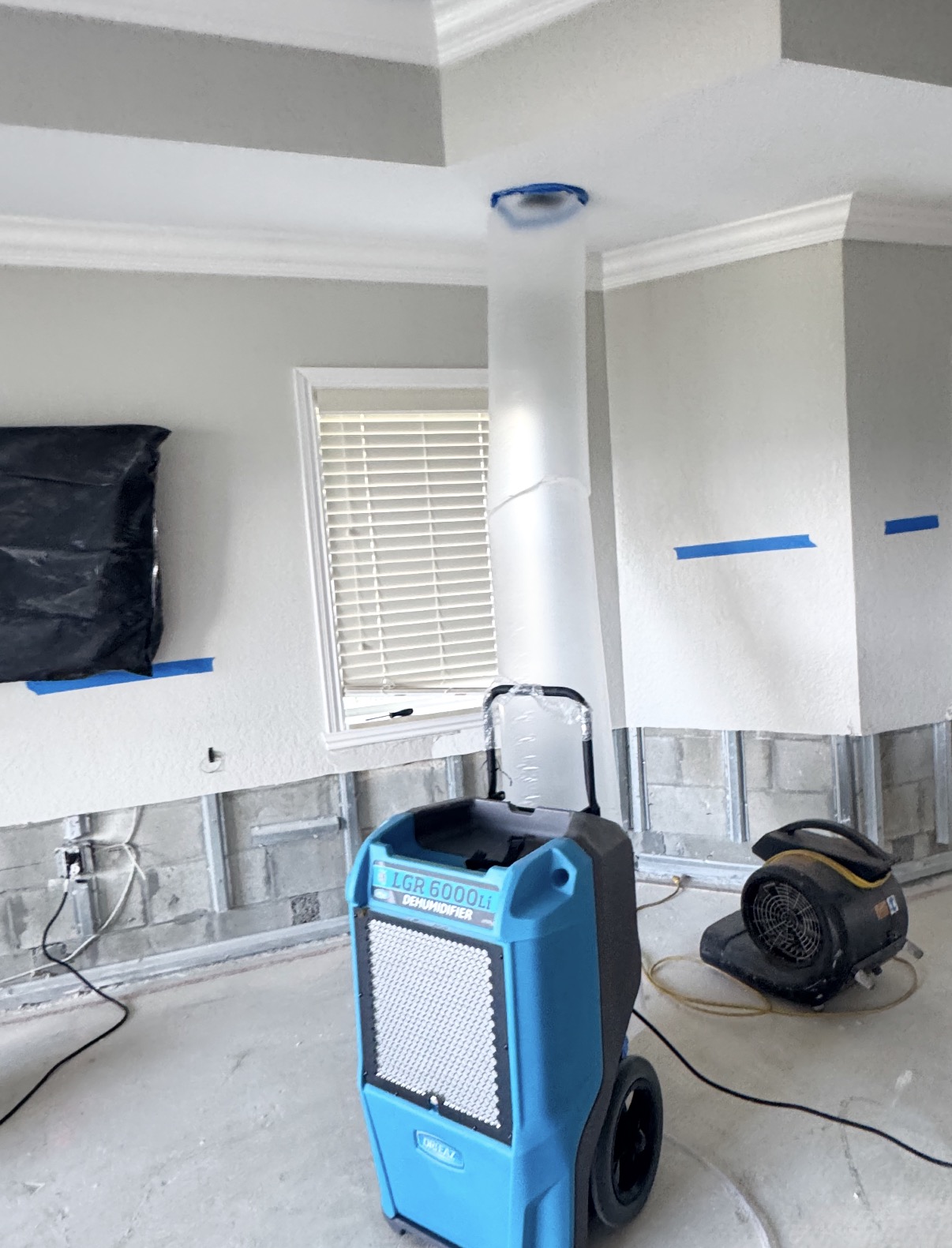 Restoration crew drying a water-damaged room with an industrial dehumidifier and air mover